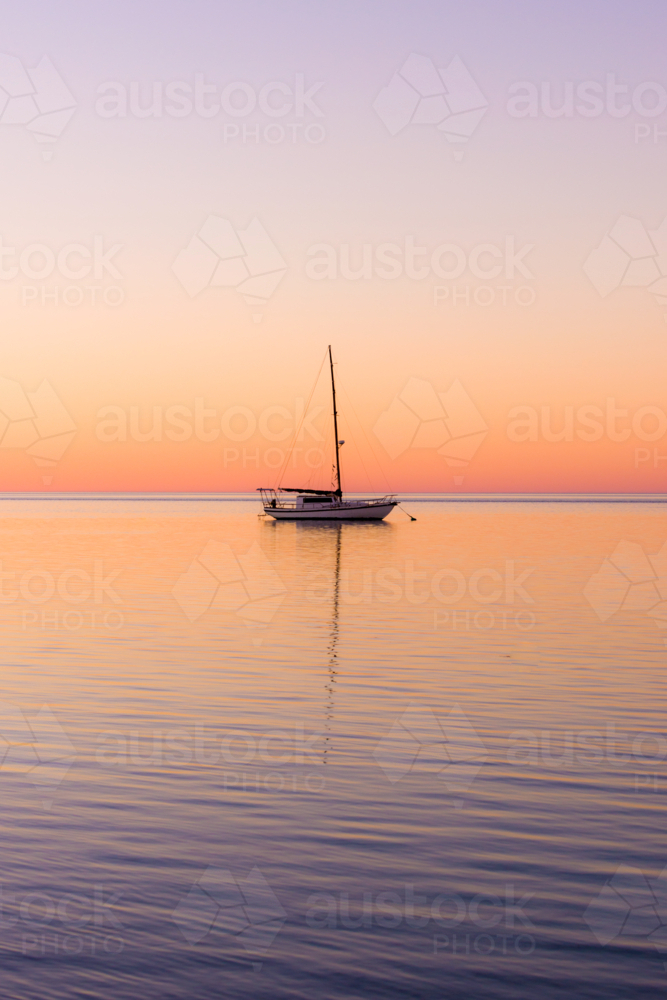 Tranquil yacht anchored at sea during a colourful sunset. - Australian Stock Image