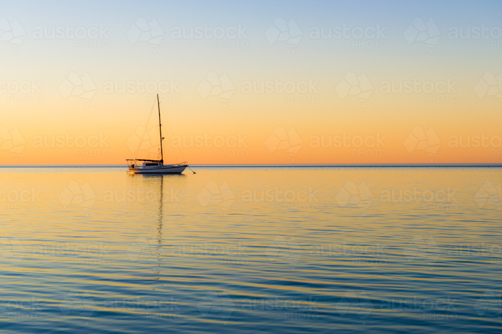 Tranquil yacht anchored at sea during a colourful sunset - Australian Stock Image