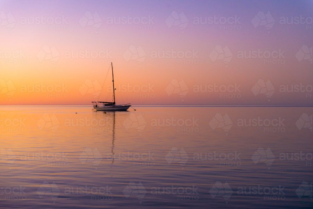 Tranquil yacht anchored at sea during a colourful sunset - Australian Stock Image