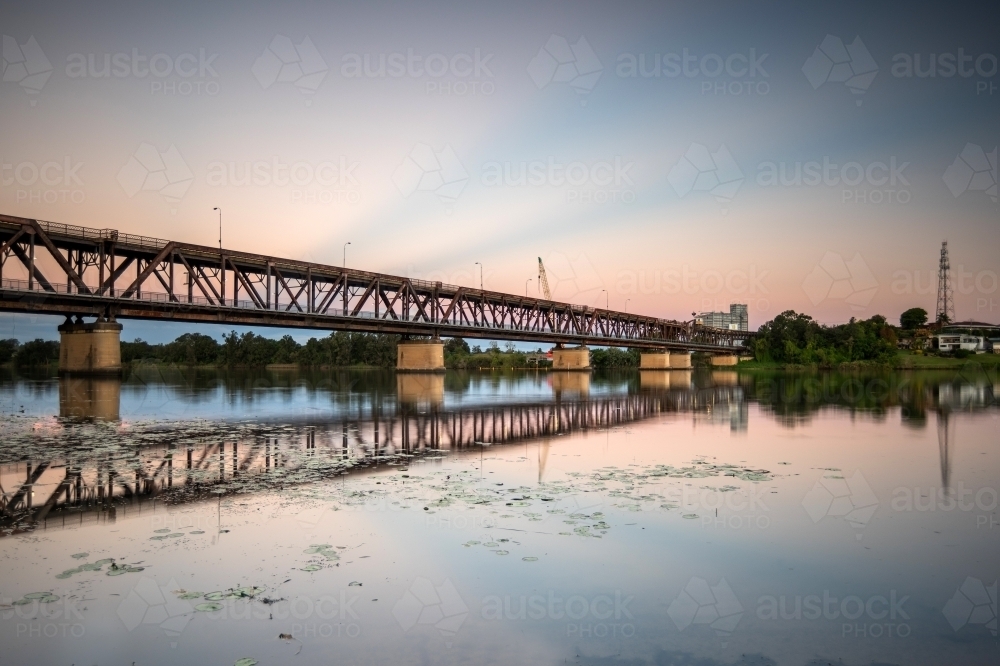Transport bridge over a river with coloured rays in the sky from sunset - Australian Stock Image