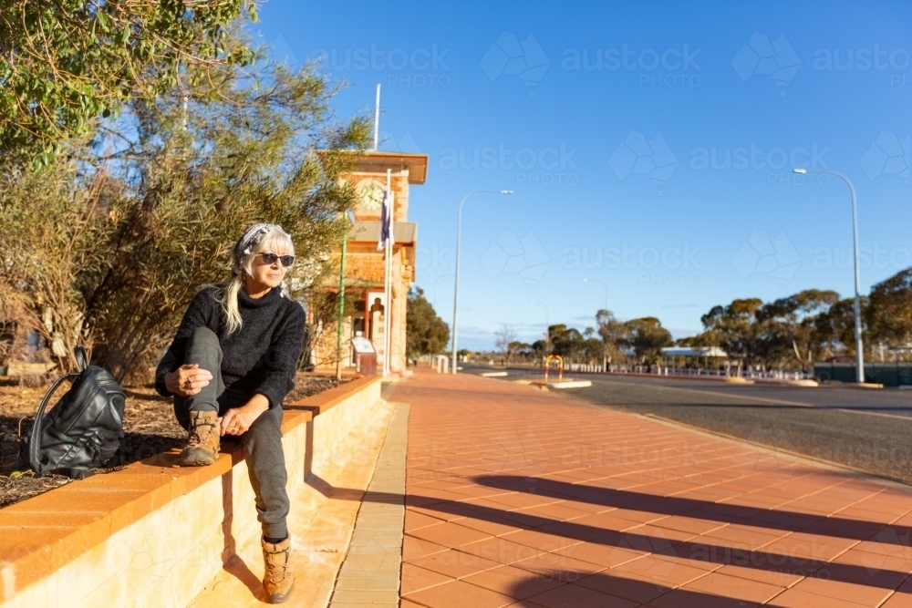 traveller sitting on wall adjusting hiking boot - Australian Stock Image