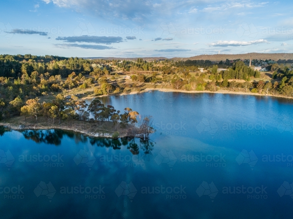 Trees at lakes edge reflecting in blue water of old quarry - Australian Stock Image