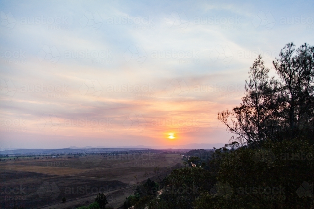 Trees silhouetted against smoke filled sunset sky - Australian Stock Image