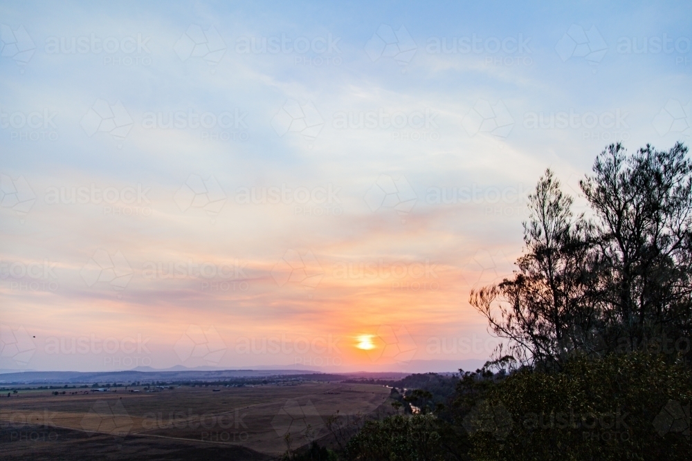 Trees silhouetted against smoke filled sunset sky - Australian Stock Image