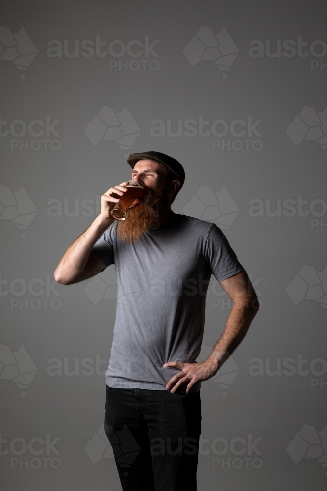 Trendy guy holding a glass of beer, relaxed and happy - Australian Stock Image