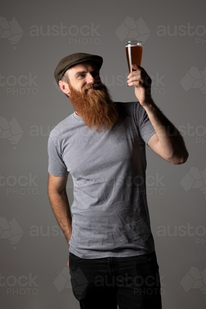 Trendy guy holding a glass of beer, relaxed and happy - Australian Stock Image