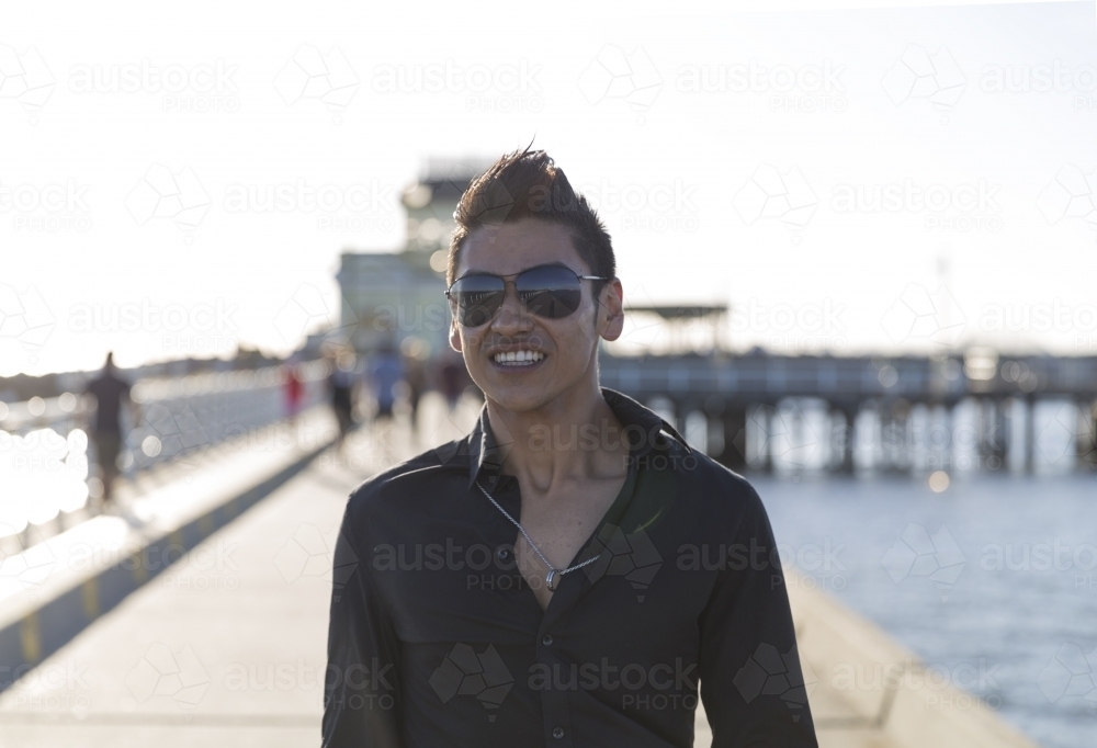Trendy young hispanic man walking along pier - Australian Stock Image