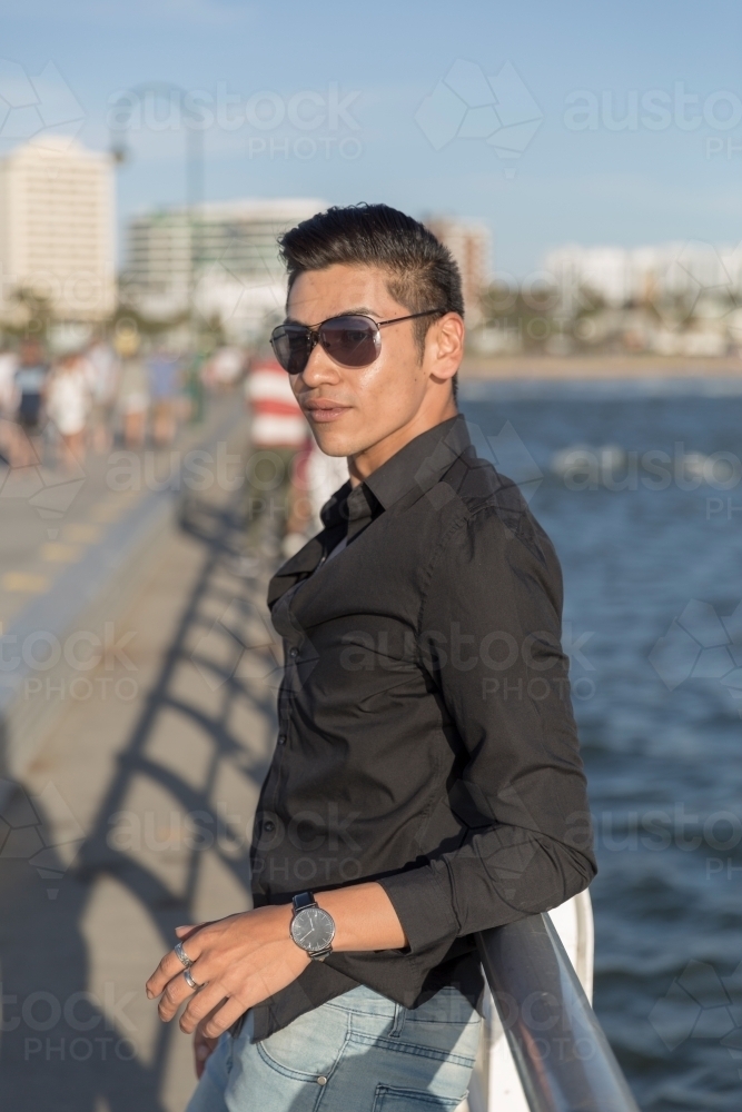 Trendy young man leaning against railing - Australian Stock Image