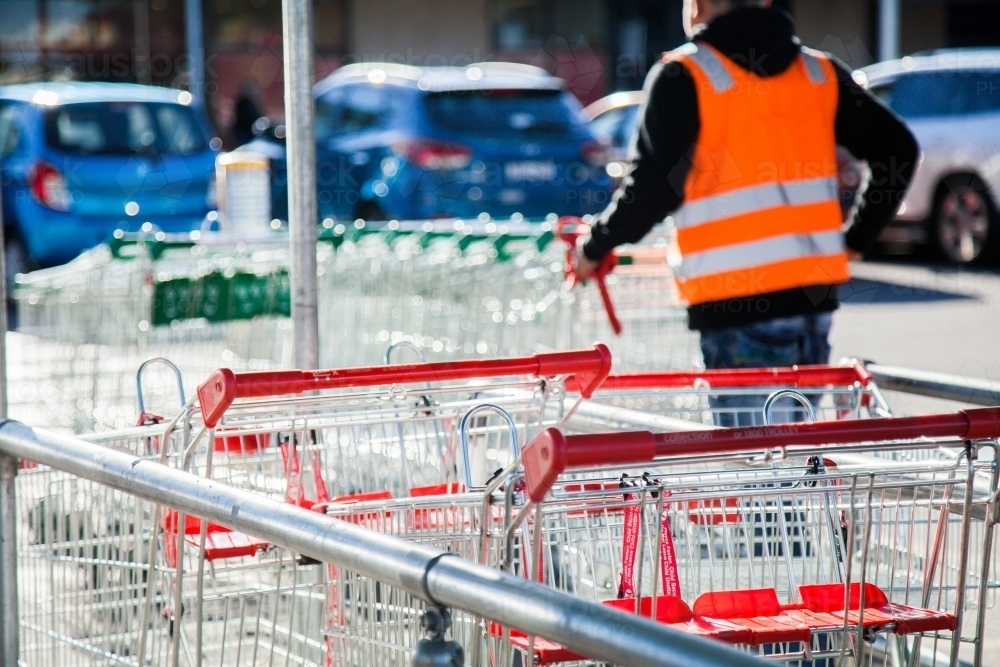 Trolley man collecting shopping trolleys from car parking lot - Australian Stock Image
