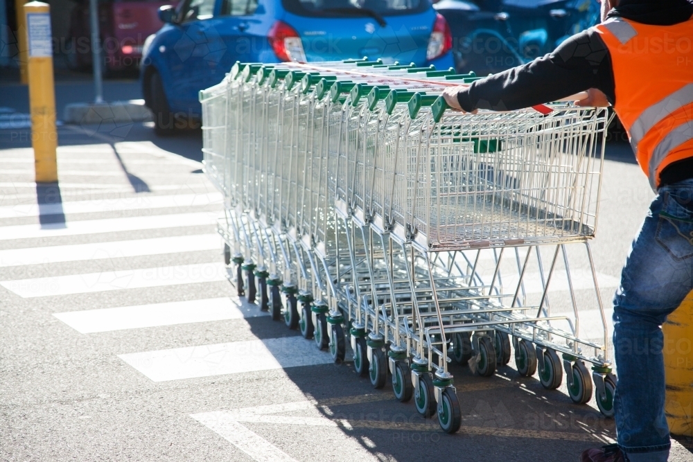 Trolley man collecting shopping trolleys from car parking lot - Australian Stock Image