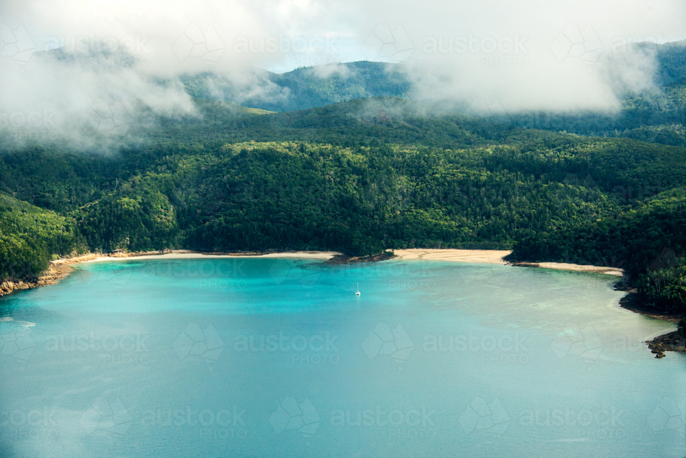 Tropical bay with turquoise water and beaches surrounded by lush rainforest and misty hills - Australian Stock Image
