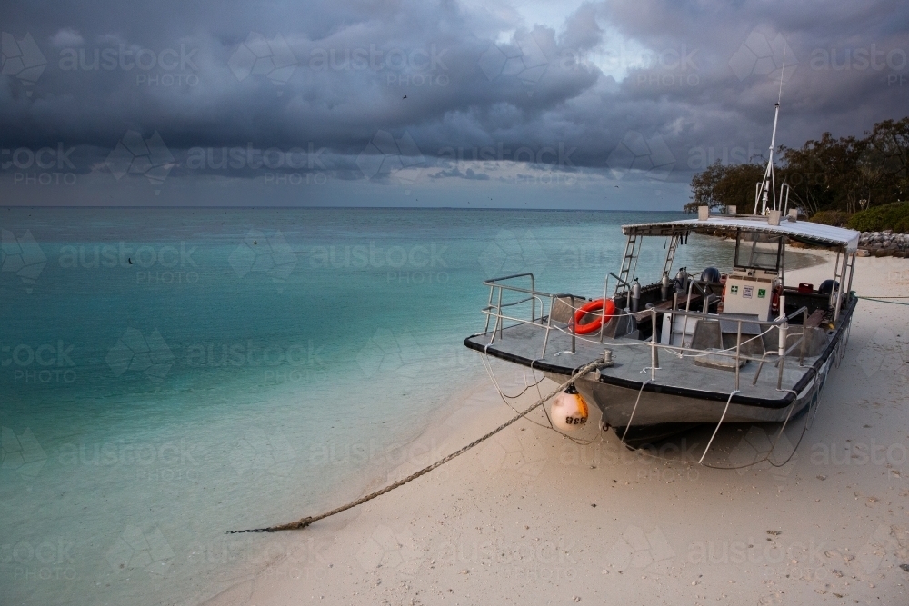 Tropical storms coming towards Heron Island with a dive boat tied up on the beach - Australian Stock Image