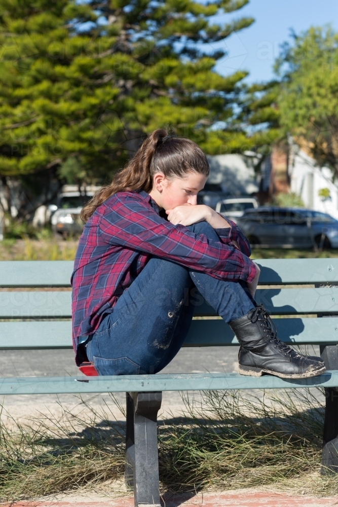 Troubled teenager sitting on park bench - Australian Stock Image