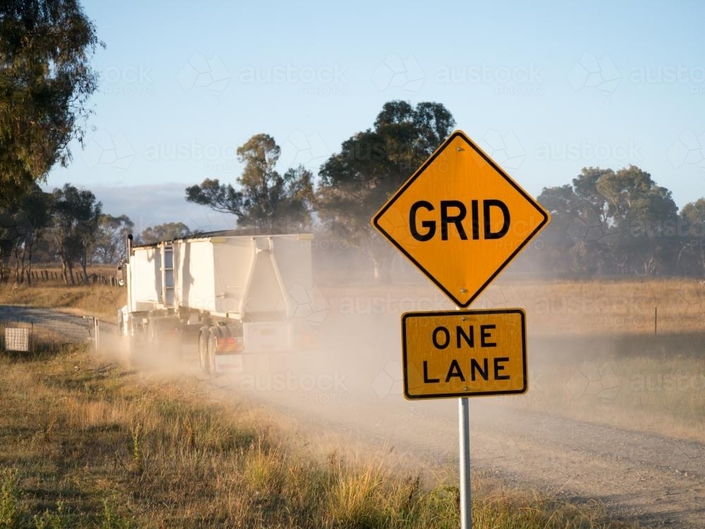Truck and trailer with dust passing a "GRID" and "ONE LANE" sign - Australian Stock Image