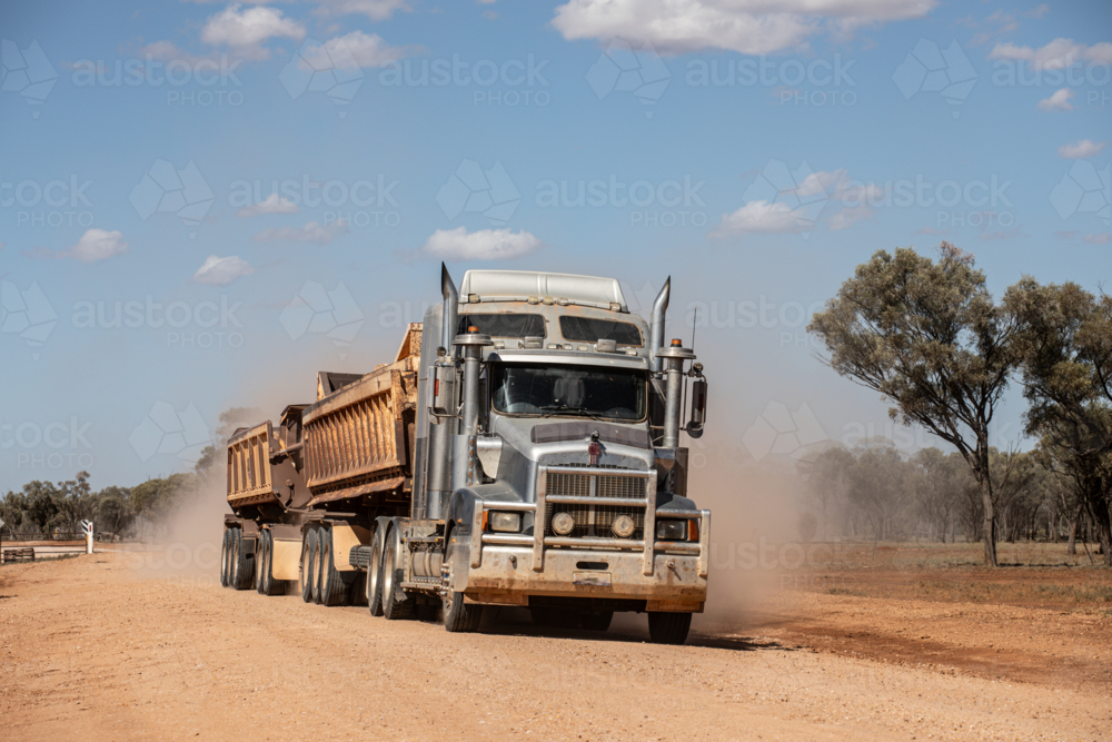 Truck pulling side tippers of gravel along a dirt road - Australian Stock Image