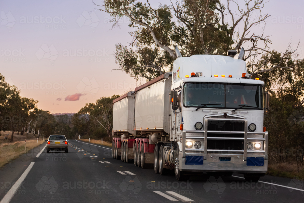 truck transporting goods on highway at dusk through Australian country passing car - Australian Stock Image