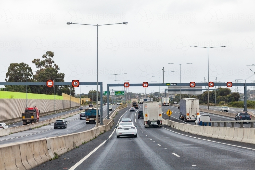trucks and cars on busy multi lane road in Melbourne, Victoria with variable speed limit signs - Australian Stock Image