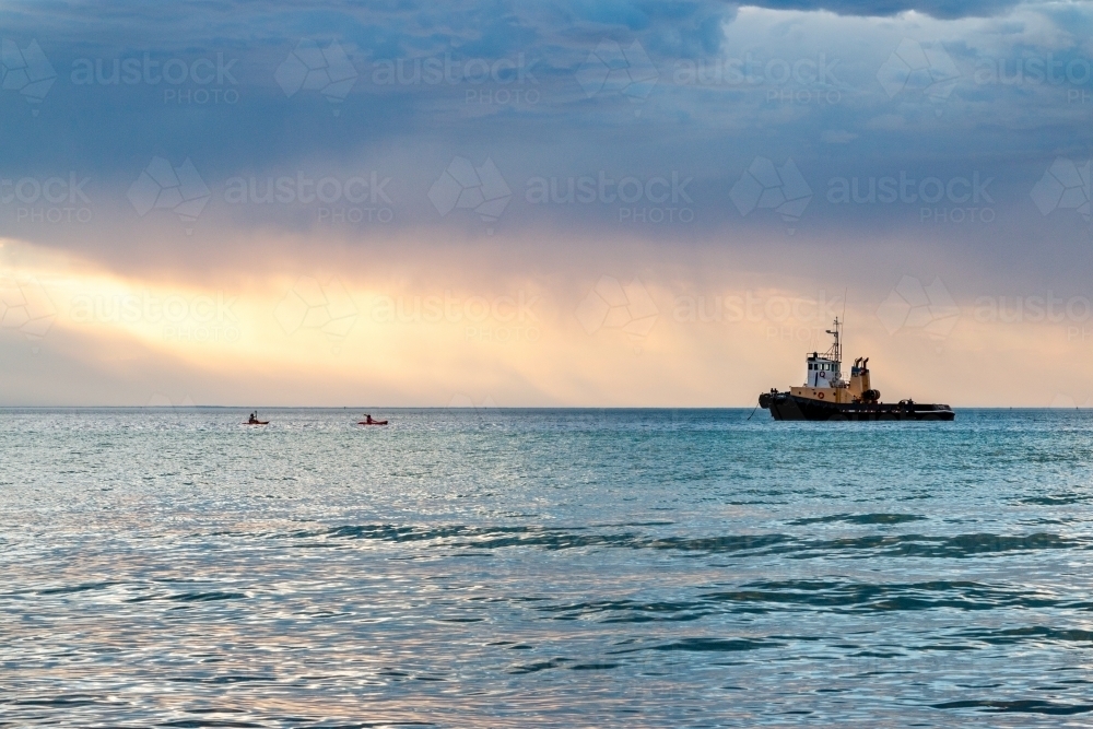 tug boat moored in bay with stormy clouds at sunset - Australian Stock Image