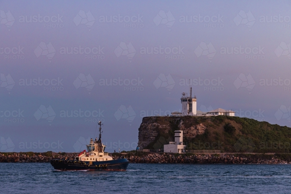 Tugboat passing Nobbys Lighthouse on the headland at the entrance to Newcastle on the Hunter River - Australian Stock Image