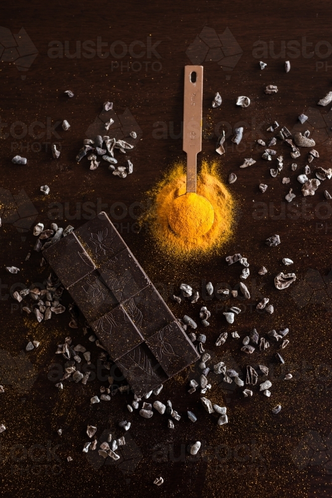 turmeric powder in a spoon, with cocoa nibs and dark chocolate - Australian Stock Image