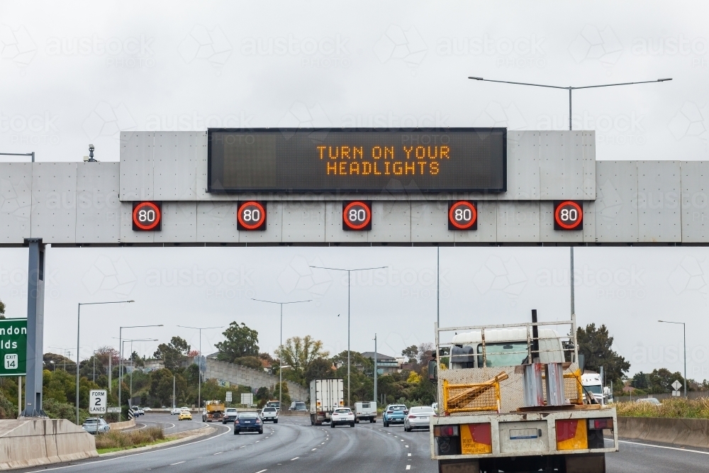Turn on your headlights sign above busy road on overcast day - Australian Stock Image