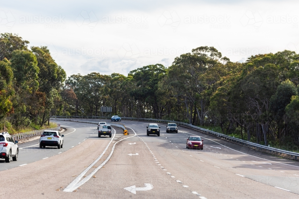 Turning lanes on road surrounded by gum trees with cars traveling past - Australian Stock Image