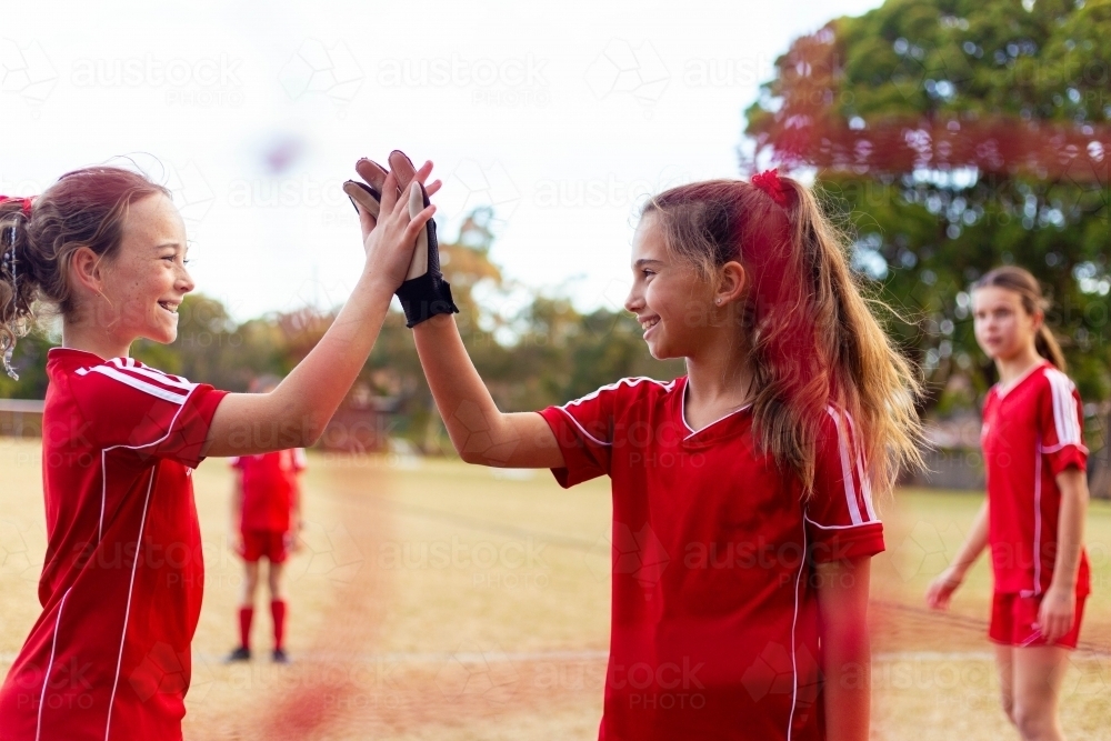 Tween female soccer players high-five in front of the goal net - Australian Stock Image