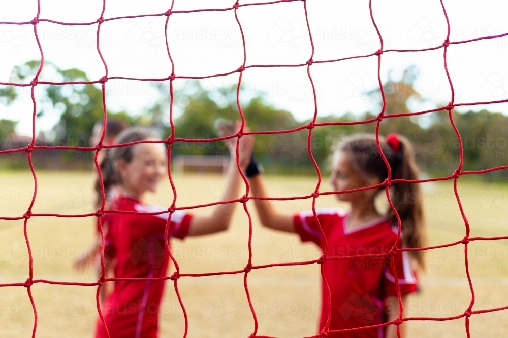 Tween female soccer players high-five in front of the goal net - Australian Stock Image