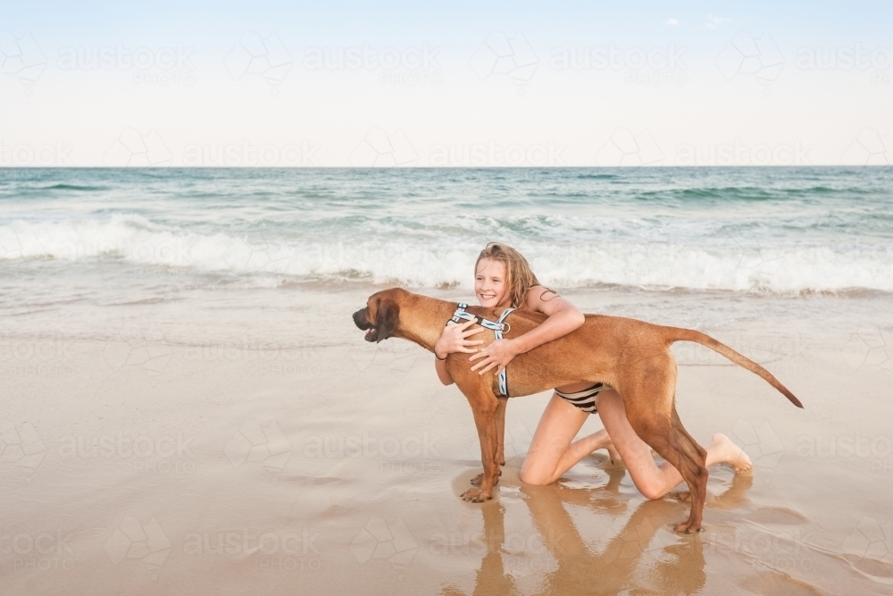 Tween girl at the beach hugging her dog - Australian Stock Image