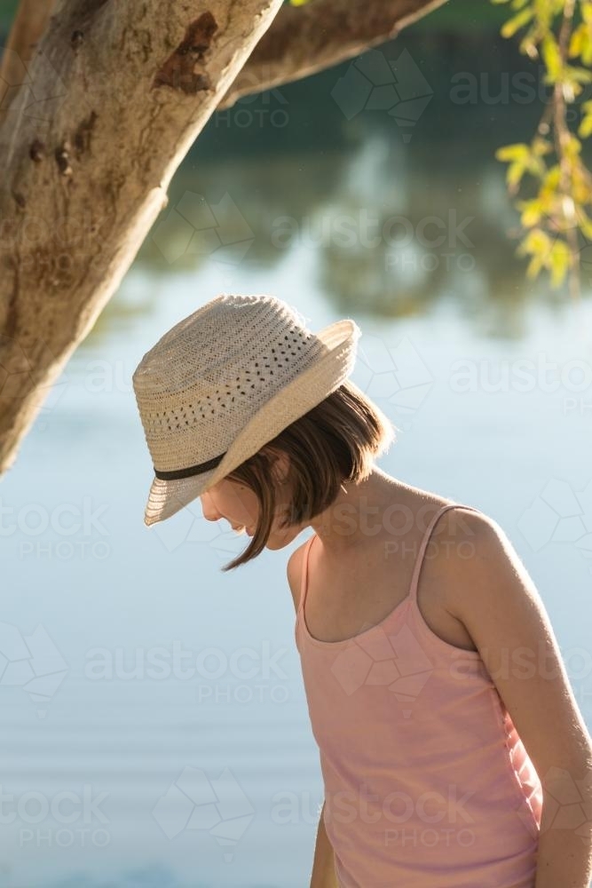 Tween girl by a river in late afternoon sunlight, looking away from camaera - Australian Stock Image