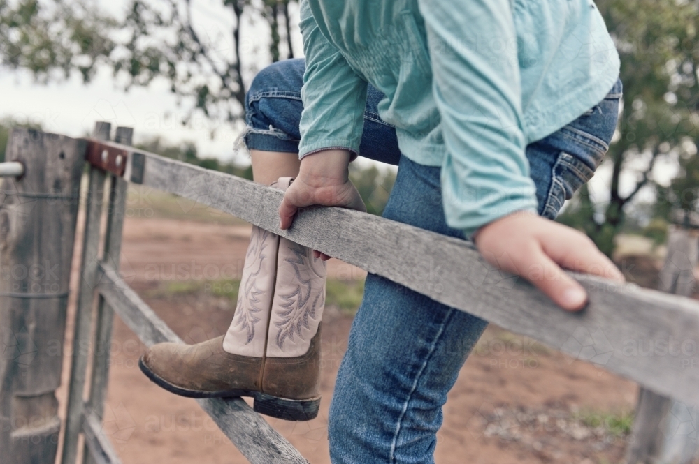 Tween girl climbing a timber fence on a rural property - Australian Stock Image