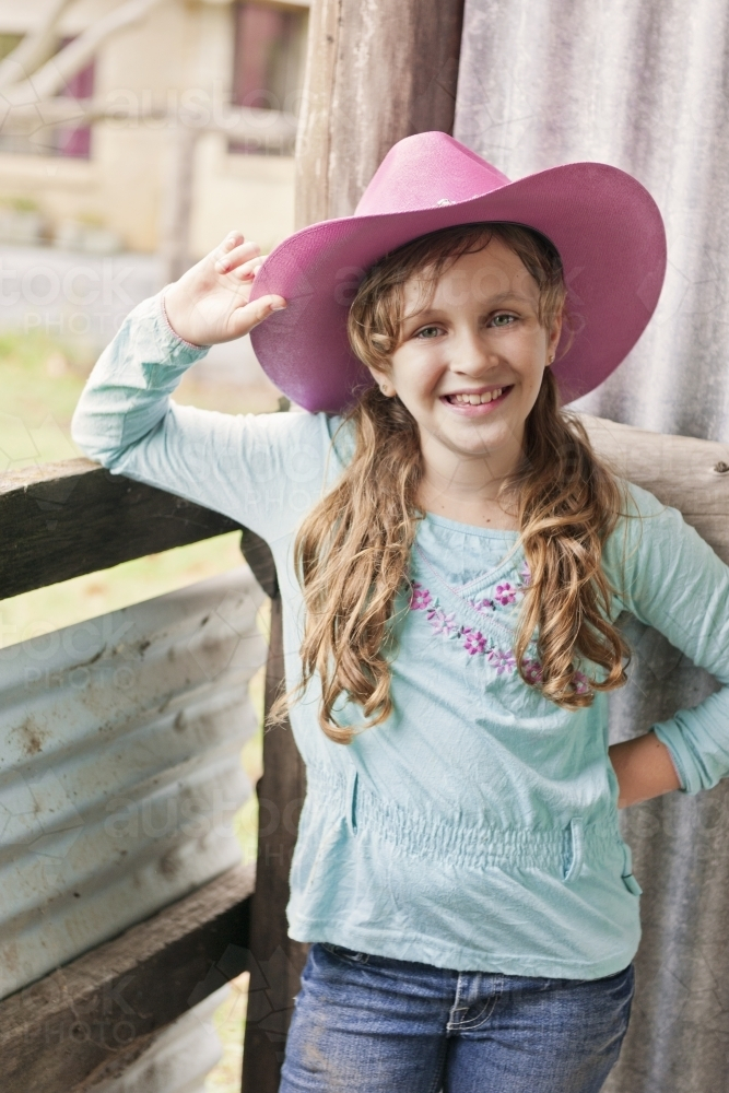 Tween girl in a pink cowgirl hat leaning on wooden fence - Australian Stock Image