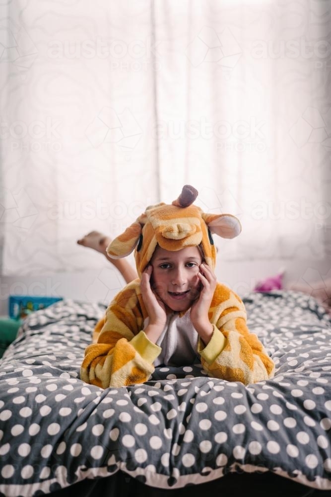 tween girl in pjs, lying on her bed, looking to camera - Australian Stock Image