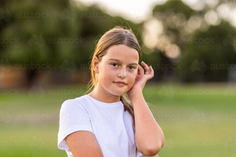 tween girl in white tee-shirt pushing hair behind her ear with one hand - Australian Stock Image