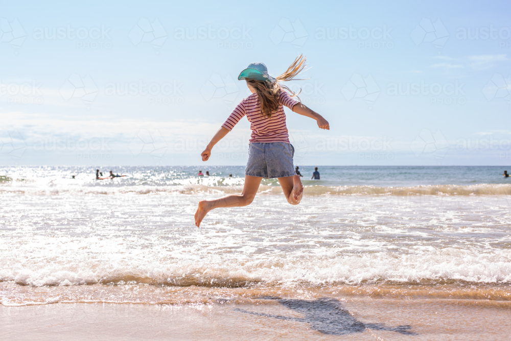tween girl jumping over waves at the beach - Australian Stock Image