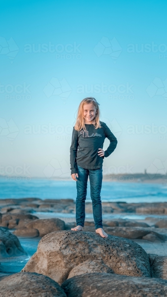 Tween girl standing on rock at the beach - Australian Stock Image