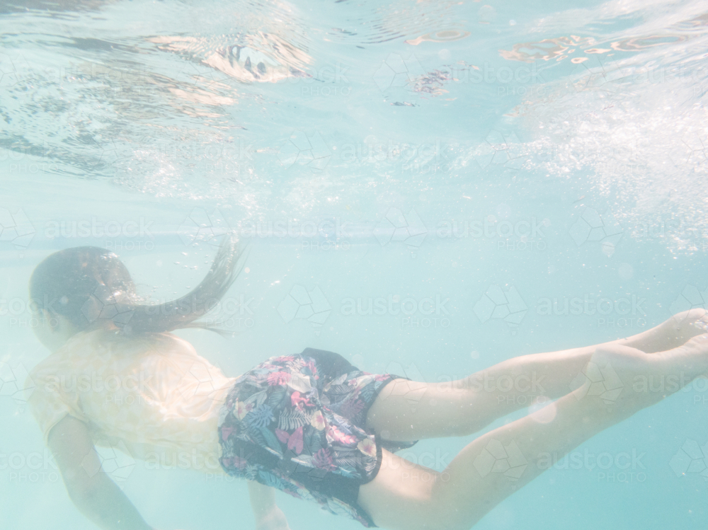 Tween girl swimming underwater in backyard pool water in summer - Australian Stock Image