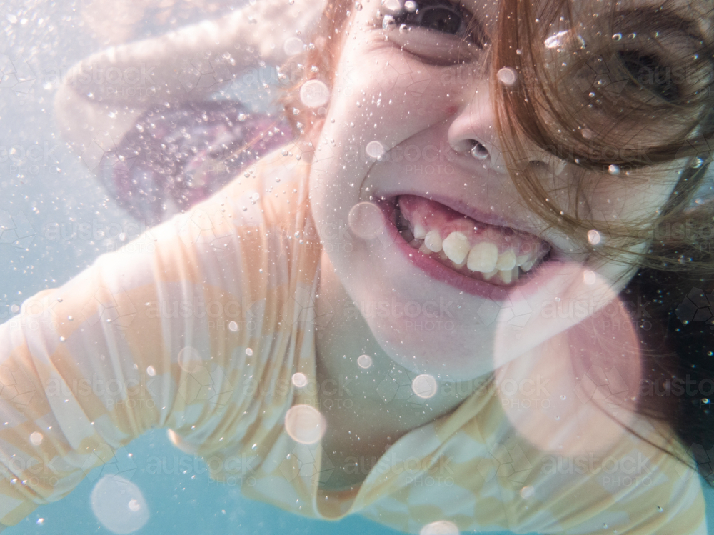 Tween girl swimming underwater in backyard pool water in summer with bubbles and hair over face - Australian Stock Image