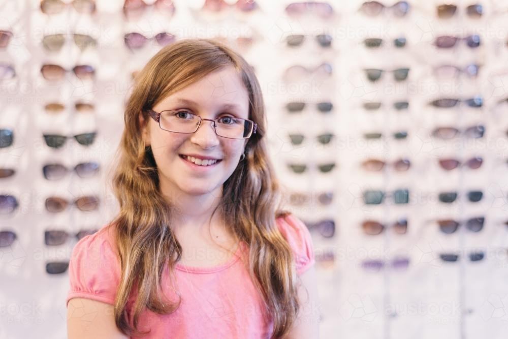 tween girl trying on glasses at optometrist - Australian Stock Image