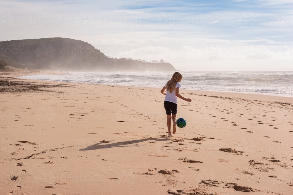 Tween girl with a ball running along sandy beach - Australian Stock Image