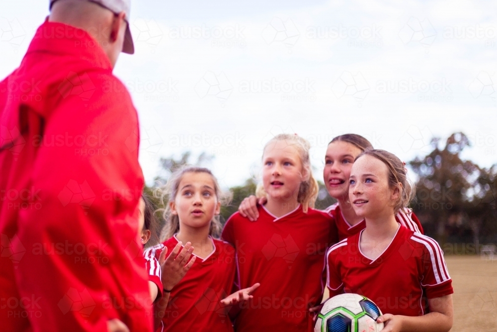 Tween soccer players in a red uniform listening to their coach - Australian Stock Image