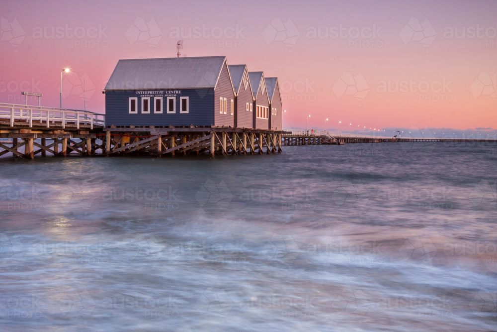 Twilight colours over a swirling sea and buildings on a long wooden jetty - Australian Stock Image