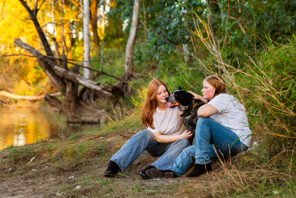 Twin teen girls with their blue heeler Australian cattle dog pet by riverside - Australian Stock Image