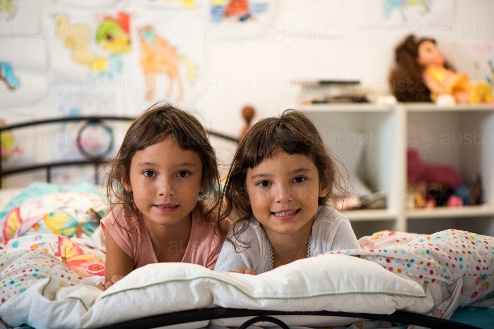 Twins sharing in their bedroom smiling on a bed. - Australian Stock Image