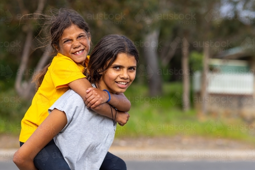 two aboriginal kids piggy-backing outdoors - Australian Stock Image