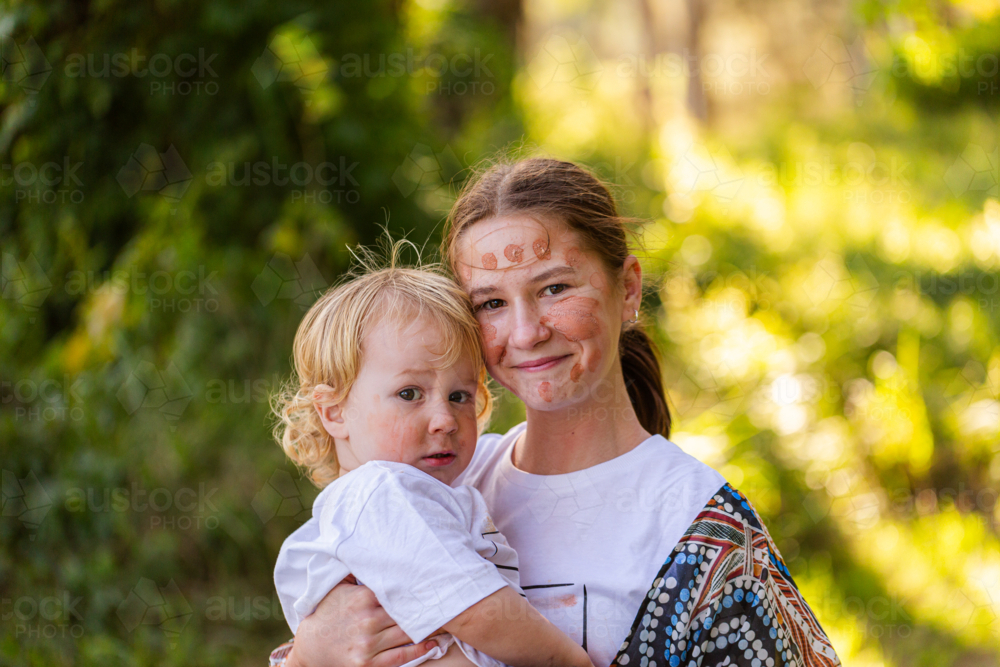 Two aboriginal siblings happy big sister and worried little brother hugging - Australian Stock Image