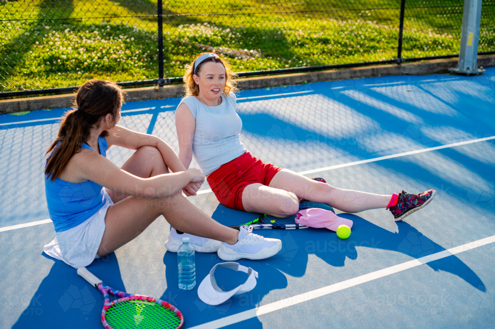 Two athletes sit on a tennis court, chatting and resting after an exciting match on a sunny day - Australian Stock Image