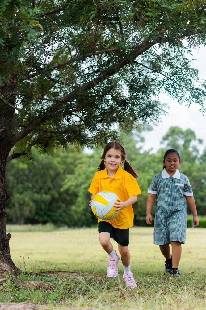 Two Australian primary school girls doing sports outside running with ball - Australian Stock Image