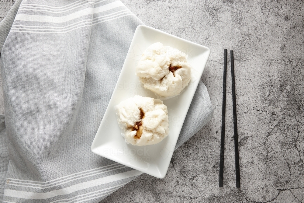 two barbecue pork buns on white plate with black chopsticks on the side - Australian Stock Image