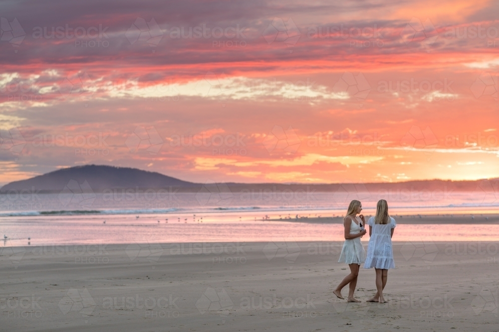 Two blonde girls in white summer dresses on a beach at sunset - Australian Stock Image